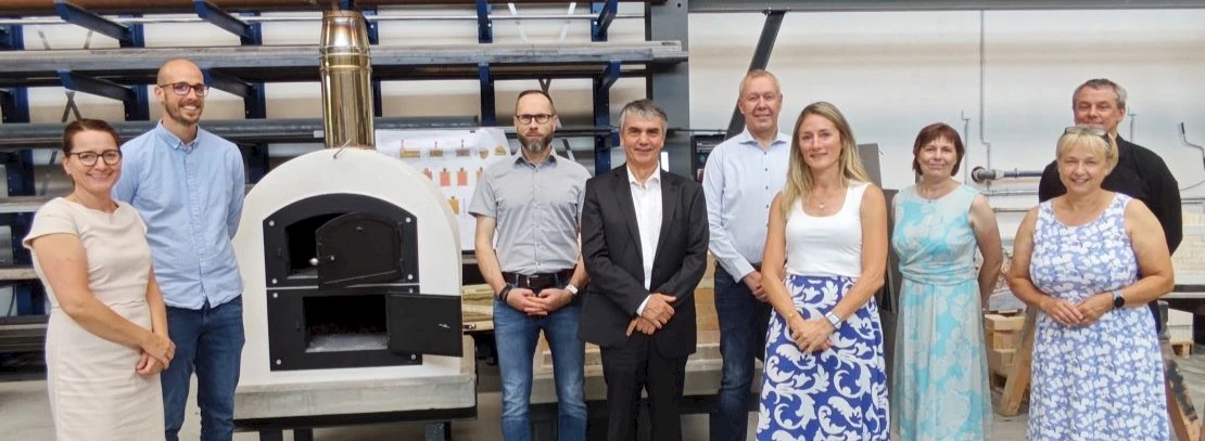 Gruppenfoto von den Besuchern der Umweltallianz und der Staatssekretär in Werkhalle neben einem Holzbackofen